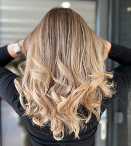 Woman with long hair showing off her ash blonde balayaged hair with dark roots and curled lengths